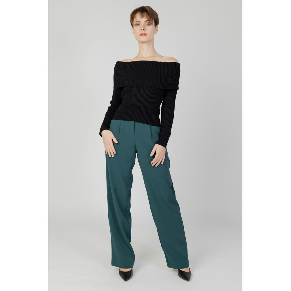 Woman modeling Vila Clothes green bootcut pants made from recycled polyester, paired with a black off-shoulder sweater. Autumn/Winter collection.