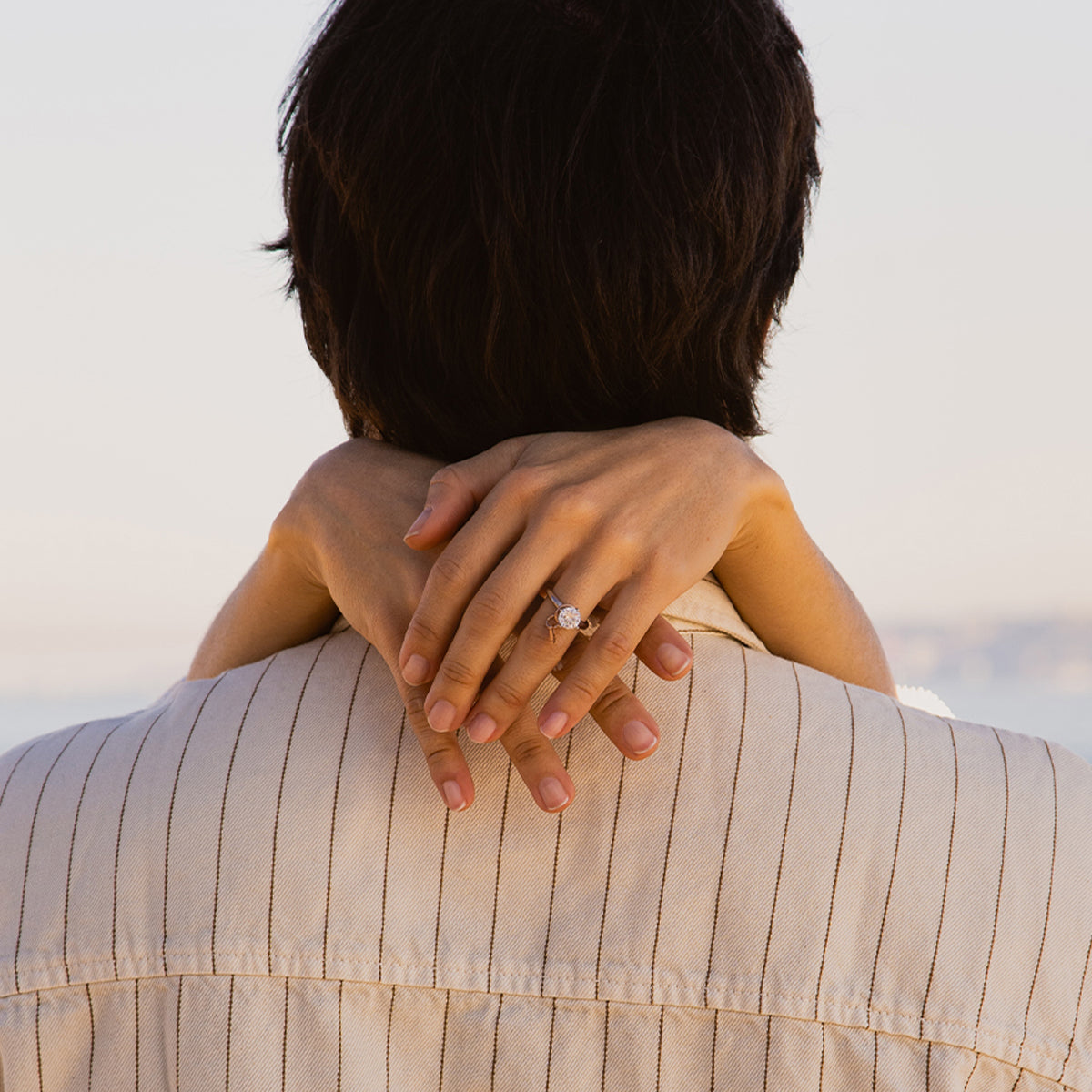 Couple embracing with a focus on a diamond ring, showcasing AN JEWELS JEWELRY Mod. AL.RLFY01-8 against a serene backdrop.