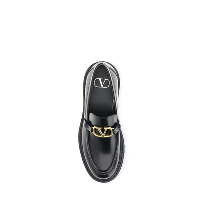 Valentino Garavani Black Leather Slip-On Loafers with VLogo and antique brass finish, featuring rubber lug sole for stability and comfort.